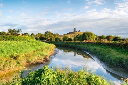 Flat ground of the Somerset Levels wetlands with Burrow Mump hill with monument on it in the distance